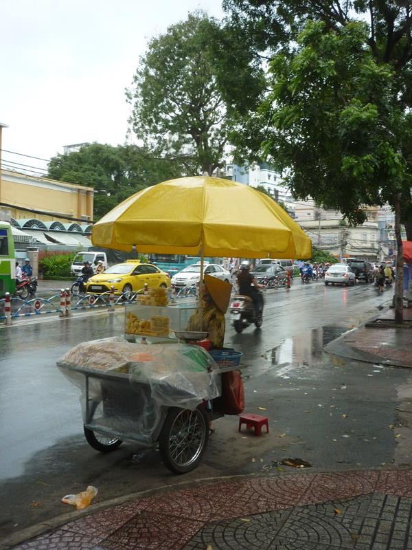 A street food vendor takes shelter from the rain
